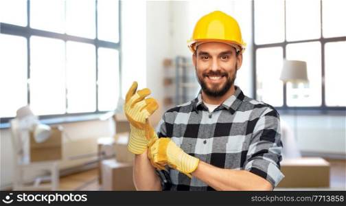 repair, construction and building concept - happy smiling male worker or builder in helmet and gloves over home room background. happy male builder in helmet and gloves at home