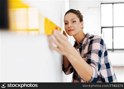repair, construction and building concept - happy smiling woman with level measuring wall at home. happy woman with level measuring wall at home