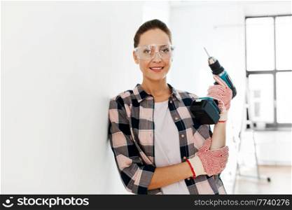 repair, construction and building concept - smiling woman or builder in goggles with perforator at home. woman in goggles with perforator at home