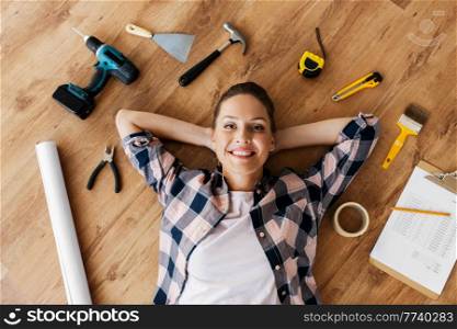 repair, construction and building concept - smiling woman with working tools and clipboard lying on wooden floor. woman with working tools lying on wooden floor