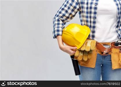 repair, construction and building concept - woman or builder with helmet and working tools on belt over grey background. woman or builder with helmet and working tools