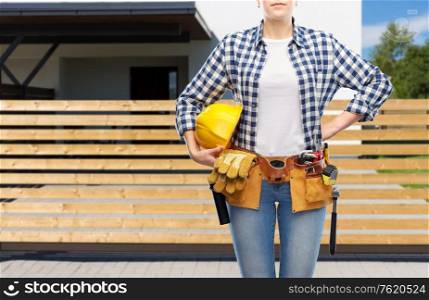 repair, construction and building concept - woman or builder with helmet and working tools on belt over living house background. woman or builder with helmet and working tools