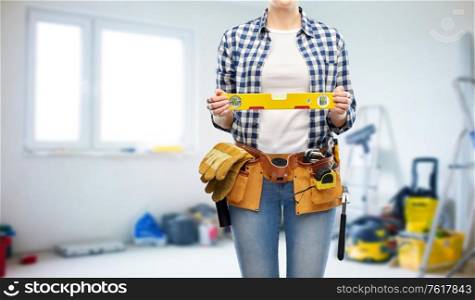 repair, construction and building concept - woman or builder with level and working tools on belt over room with equipment background. woman builder with level and working tools on belt