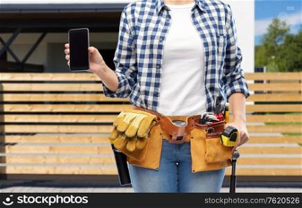 repair, construction and building concept - woman or builder with smartphone and working tools on belt over living house background. woman or builder with phone and working tools