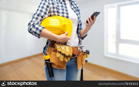 repair, construction and building concept - woman or builder with smartphone, helmet and working tools on belt over empty room at new home background. woman or builder with phone and working tools