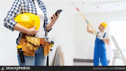 repair, construction and building concept - woman or builder with smartphone, helmet and working tools on belt over painter painting ceiling background. woman or builder with phone and working tools