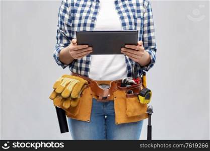 repair, construction and building concept - woman or builder with tablet pc computer working tools on belt over grey background. woman or builder with tablet pc and working tools