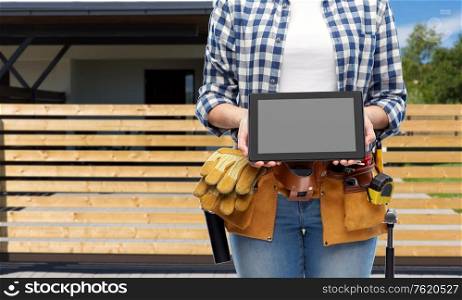 repair, construction and building concept - woman or builder with working tools on belt showing tablet pc computer over living house background. woman builder with working tools showing tablet pc
