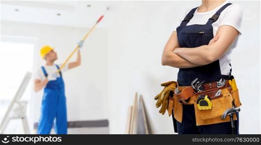 repair, construction and building concept - woman or builder with working tools on belt over painter painting ceiling background. woman or builder with working tools on belt