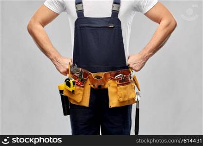 repair, construction and building - male worker or builder in overall with working tools on belt over grey background. worker or builder in overall with working tools
