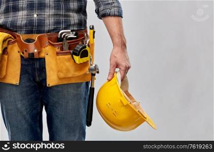 repair, construction and building - male worker or builder with helmet and working tools on belt over grey background. worker or builder with helmet and working tools