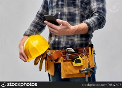 repair, construction and building - male worker or builder with smartphone and working tools on belt over grey background. worker or builder with phone and working tools