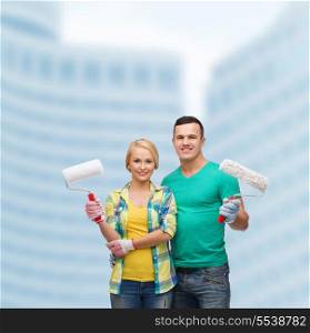 repair, construction and maintenance concept - smiling couple in gloves with paint rollers