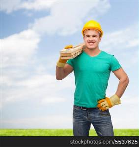 repair, construction and maintenance concept - smiling male manual worker in protective helmet carrying wooden boards