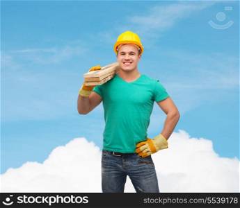 repair, construction and maintenance concept - smiling male manual worker in protective helmet carrying wooden boards
