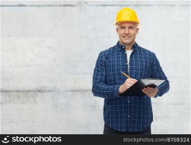 repair, construction, building, people and maintenance concept - smiling male builder or manual worker in helmet with clipboard taking notes over gray concrete wall background