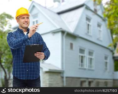 repair, construction, building, people and maintenance concept - smiling male builder or manual worker in helmet with clipboard taking notes over living house background