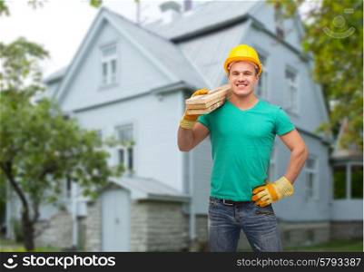 repair, construction, people, building and maintenance concept - smiling male manual worker in protective helmet carrying wooden boards over house background