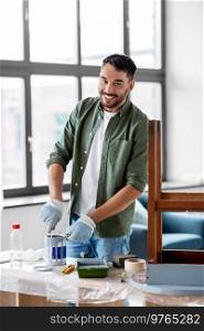 repair, diy and home improvement concept - happy smiling man in protective gloves stirring can with grey color paint for painting old wooden table. man stirring can with grey color paint at home