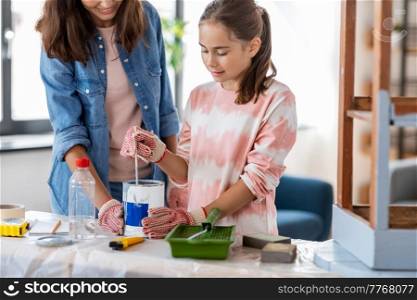 repair, diy and home improvement concept - happy smiling mother and daughter in protective gloves stirring grey color paint in can for painting old wooden table at home. mother and daughter stirring grey paint at home
