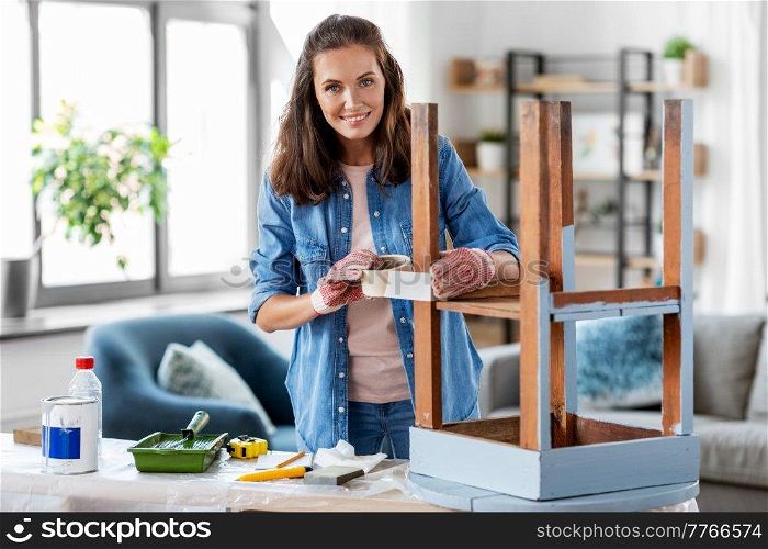 repair, diy and home improvement concept - happy smiling woman sticking adhesive tape to old wooden table for repainting it. woman sticking masking tape to table for repaint