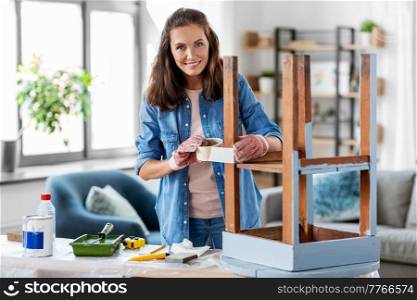 repair, diy and home improvement concept - happy smiling woman sticking adhesive tape to old wooden table for repainting it. woman sticking masking tape to table for repaint