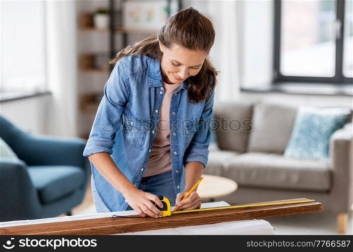 repair, diy and home improvement concept - happy smiling woman with ruler and pencil measuring wooden board at home. woman with ruler measuring wooden board at home