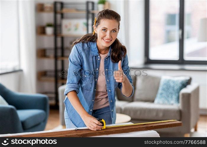 repair, diy and home improvement concept - happy smiling woman with ruler measuring wooden board at home and showing thumbs up. happy woman measuring board and showing thumbs up