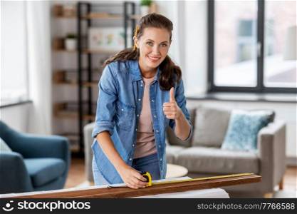 repair, diy and home improvement concept - happy smiling woman with ruler measuring wooden board at home and showing thumbs up. happy woman measuring board and showing thumbs up