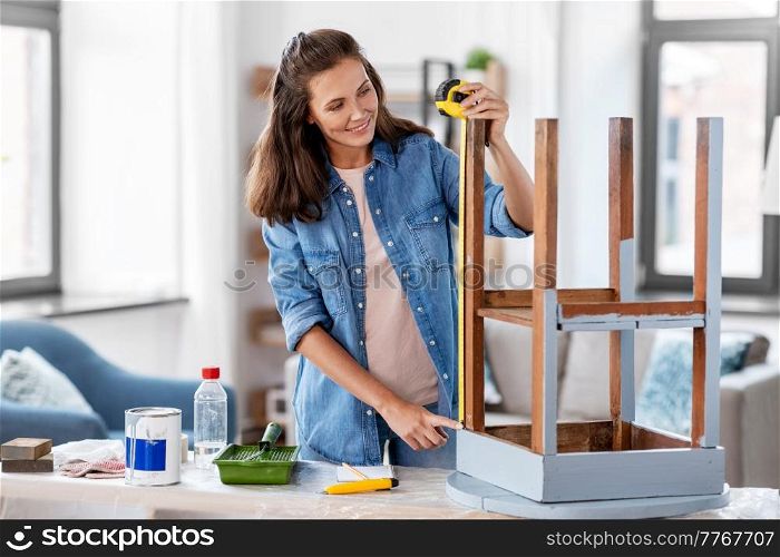 repair, diy and home improvement concept - happy smiling woman with ruler measuring old wooden table for renovation. woman with ruler measuring table for renovation