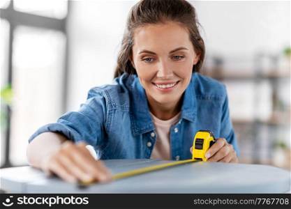 repair, diy and home improvement concept - happy smiling woman with ruler measuring old round wooden table for renovation. woman with ruler measuring table for renovation