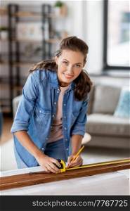 repair, diy and home improvement concept - happy smiling woman with ruler and pencil measuring wooden board at home. woman with ruler measuring wooden board at home