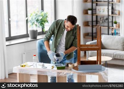 repair, diy and home improvement concept - man in protective gloves pouring grey color paint to tray for painting old wooden table. man in gloves pouring grey color paint to tray