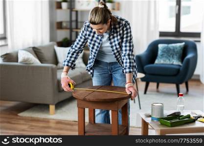 repair, diy and home improvement concept - woman with ruler measuring old wooden table for renovation. woman with ruler measuring table for renovation