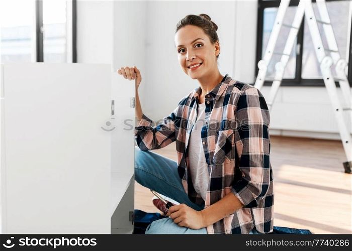 repair, improvement and furniture concept - happy smiling woman with screwdriver assembling locker at home. woman assembling furniture at home