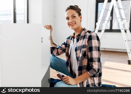 repair, improvement and furniture concept - happy smiling woman with screwdriver assembling locker at home. woman assembling furniture at home