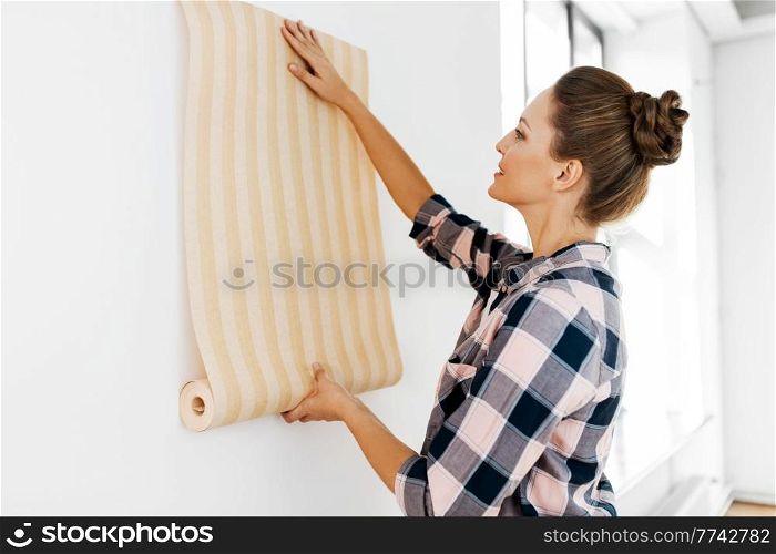 repair, improvement and renovation concept - happy smiling woman applying wallpaper to wall at home. woman applying wallpaper to wall at home