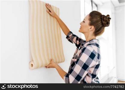 repair, improvement and renovation concept - happy smiling woman applying wallpaper to wall at home. woman applying wallpaper to wall at home
