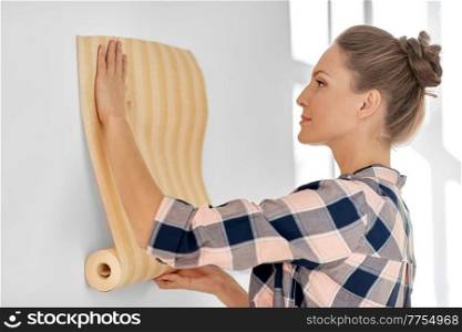 repair, improvement and renovation concept - woman applying wallpaper to wall at home. woman applying wallpaper to wall at home