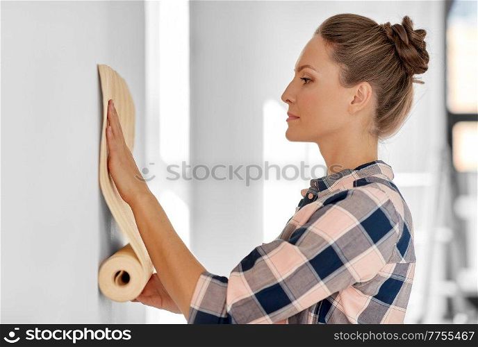 repair, improvement and renovation concept - woman applying wallpaper to wall at home. woman applying wallpaper to wall at home