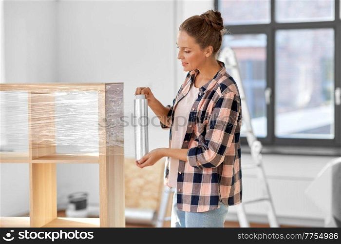 repair, people and real estate concept - smiling happy woman packing shelf with plastic wrap and moving to new home. happy woman packing shelf and moving to new home
