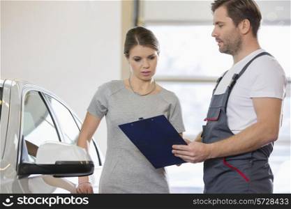 Repairman holding clipboard while conversing with female customer in repair shop