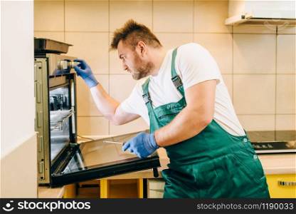 Repairman in uniform checks the oven, technician. Professional worker makes repairs around the house, home repairing service. Repairman in uniform checks the oven, technician