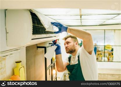 Repairman in uniform cleans the air conditioner, handyman. Professional worker makes repairs around the house, home repairing service. Repairman in uniform cleans the air conditioner