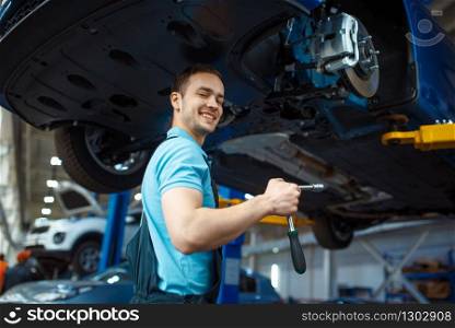 Repairman in uniform repairing vehicle on lift, car service station. Automobile checking and inspection, professional diagnostics and repair. Repairman repairing vehicle on lift, car service