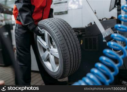 Repairman puts the wheel on the balancing machine, tire service. Man repairs car tyre in garage, automobile on lift jack, inspection in workshop