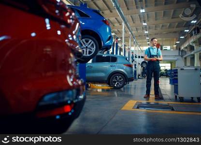 Repairman stands at vehicles on lifts, car service station. Automobile checking and inspection, professional diagnostics and repair. Repairman stands at vehicles on lifts, car service
