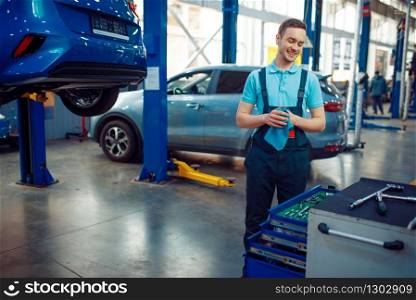 Repairman stands at vehicles on lifts, car service station. Automobile checking and inspection, professional diagnostics and repair. Repairman stands at vehicles on lifts, car service