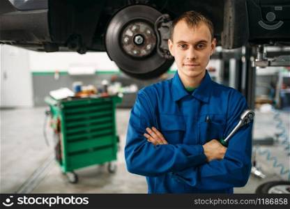 Repairman with wrench against a car on the lift, suspension diagnostic. Automobile service, vehicle maintenance