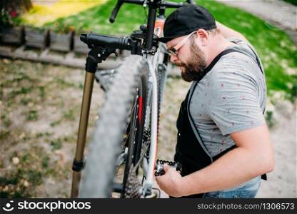 Repairman works with bike wheel, cycle workshop outdoor. Bearded bicycle mechanic in apron. Repairman works with bike wheel, cycle workshop